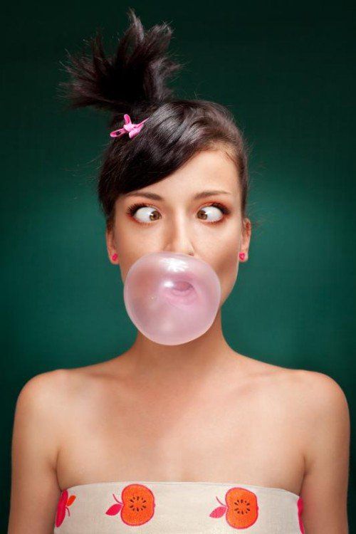 a beautiful brunette with squint eyed blowing a bubblegum on a green background