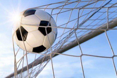 Fußball fliegt vor blauen Himmel ins Tor, mit Gegenlicht
