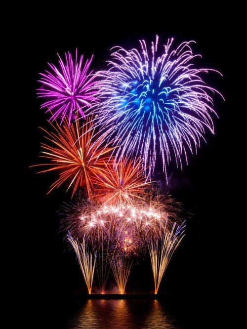 Prachtvolles buntes Feuerwerk auf Schwarz mit Reflektion auf Wasser