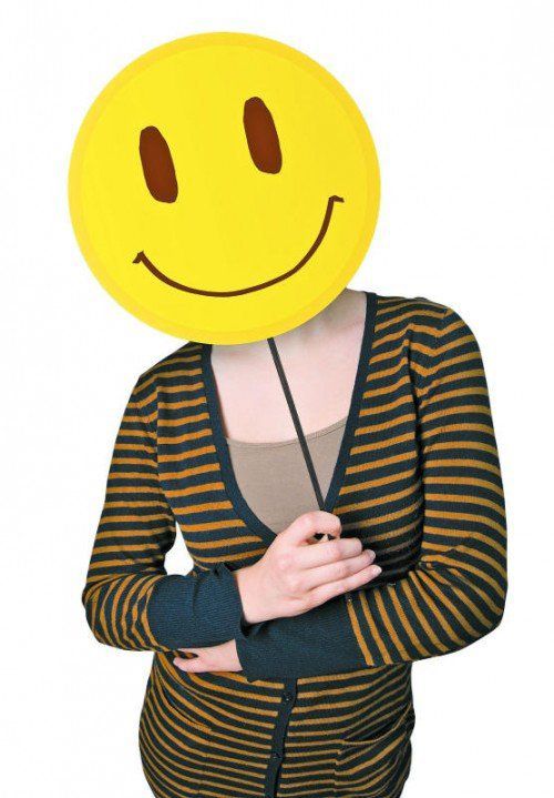 Young lady holding a yellow smiley face emoticon in front of her head