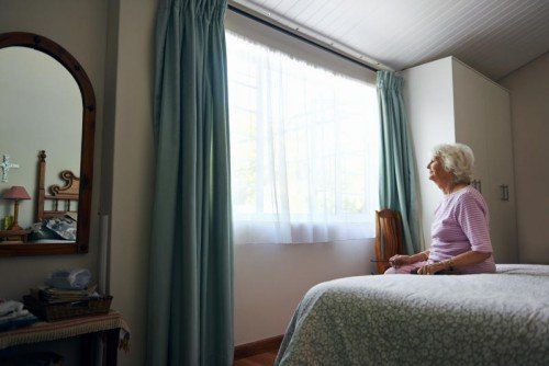 A depressed elderly widow sitting on her bed looking out the window