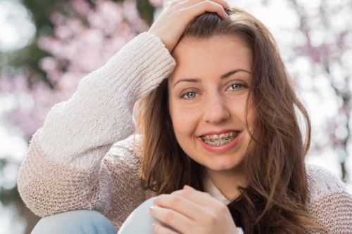 Happy girl wearing braces with hand in hair outdoors spring