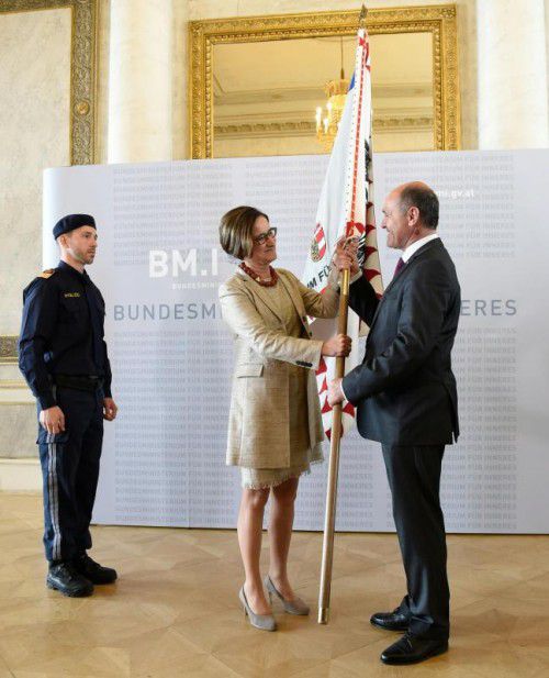 Johanna Mikl-Leitner übergibt ihr Innenressort mit der Fahne des Ministeriums symbolisch an Wolfgang Sobotka. 