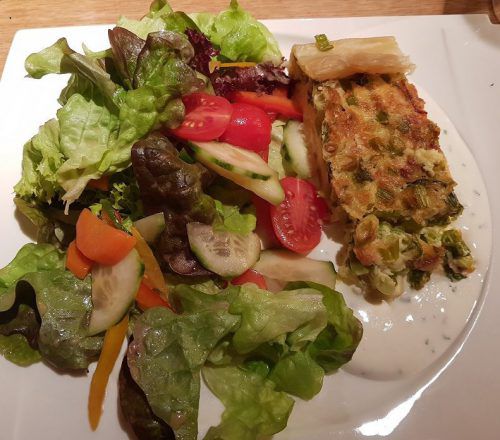 Die Quiche mit Frühlingszwiebeln und Speck an Blattsalat.