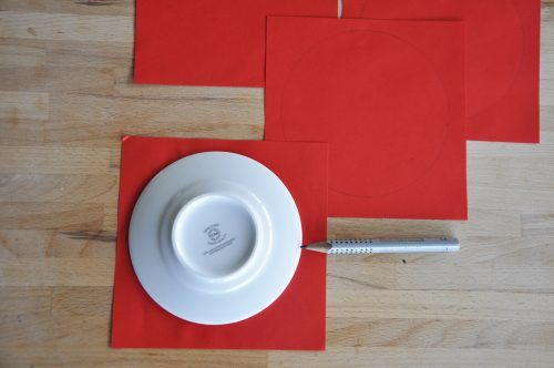 Zuerst zeichnet ihr vier Kreise auf das rote Papier auf und schneidet sie aus.
