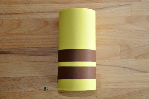 Zwei schmale Streifen aus dem braunen Papier ausschneiden und am unteren Teil der Papprolle festkleben.