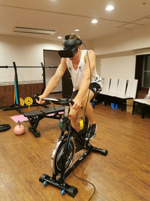 Segel-Ass Benjamin Bildstein in Japan auf dem Radergometer mit einer Virtual Reality Brille.
