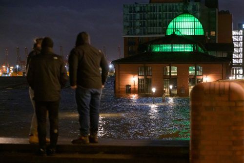 Passanten standen am Samstag am frühen Morgen vor dem überfluteten Hamburger Fischmarkt mit Fischauktionshalle an der Elbe.  APA/dpa/J. Walzberg