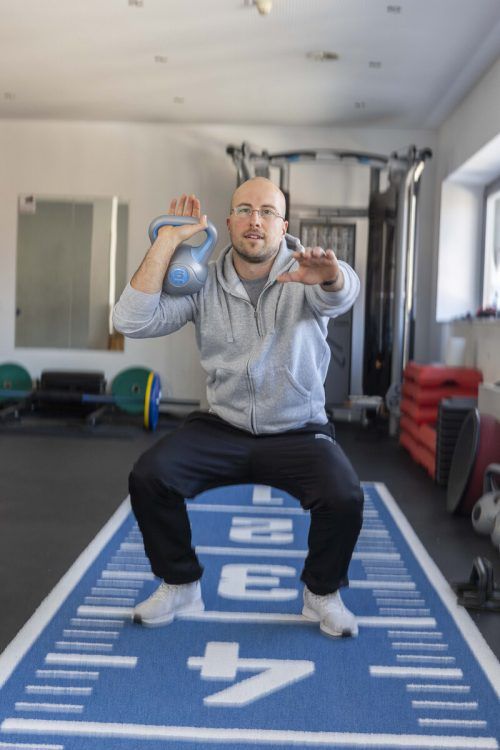 Der 34-Jährige zeigt, wie man Kniebeugen mit Kettlebells macht.