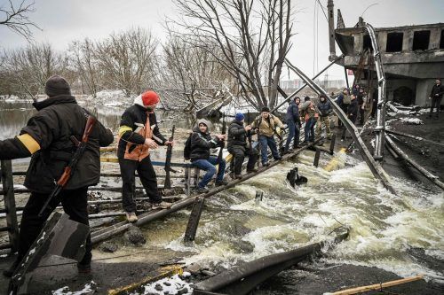 Milizionäre reichen Sturmgewehre über eine zerstörte Brücke.