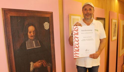Neben dem Bild von Pfarrer Brügel zeigt Ingo Metzler die Urkunde, mit der Maecenas das Kunstprojekt ausgezeichnet hat. STP/2