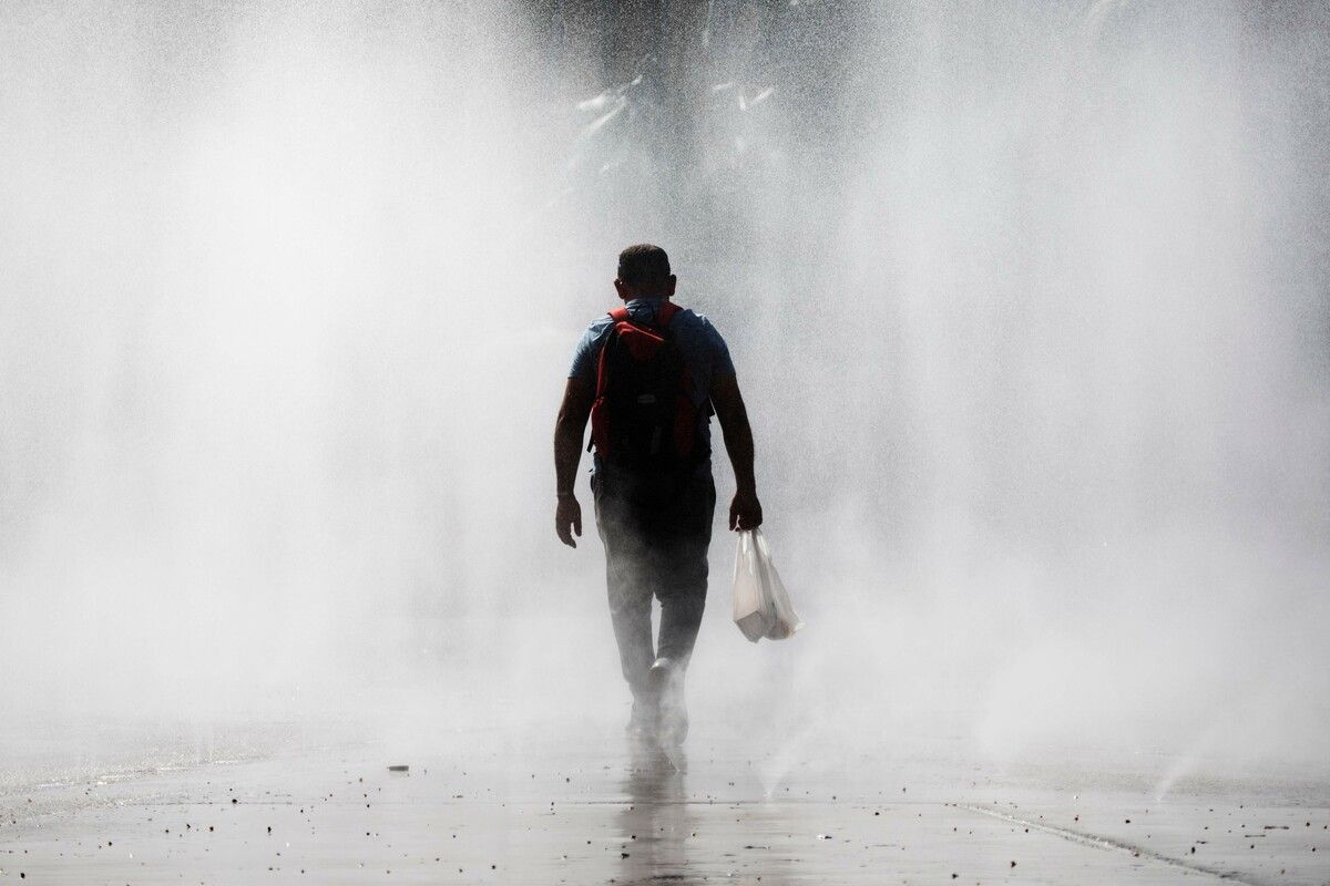 Bei Temperaturen von knapp 35 Grad geht ein Mann durch das Wasserspiel am Wiener Praterstern. AFP