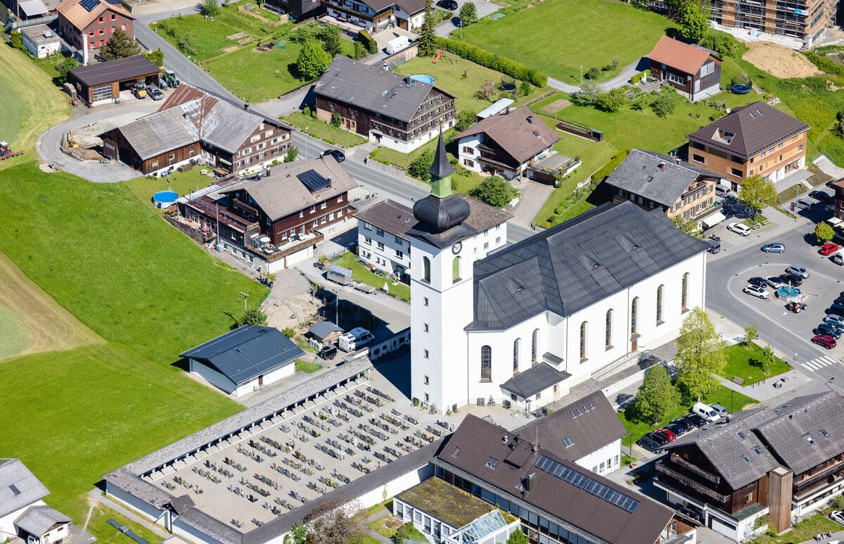 Luftbild der Pfarrkirche Hl. Drei Könige und Arkadenfriedhof mit umliegenden Häusern. Volare