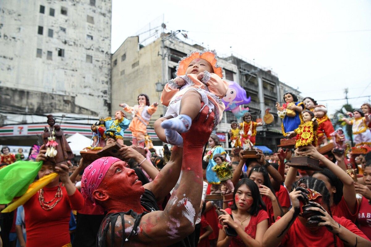 Während einer Straßenfeier in Manila auf den Philippinen hebt ein Tänzer ein Kind neben Bildern des Jesuskindes Santo Nino vor einer Kirche hoch. AFP