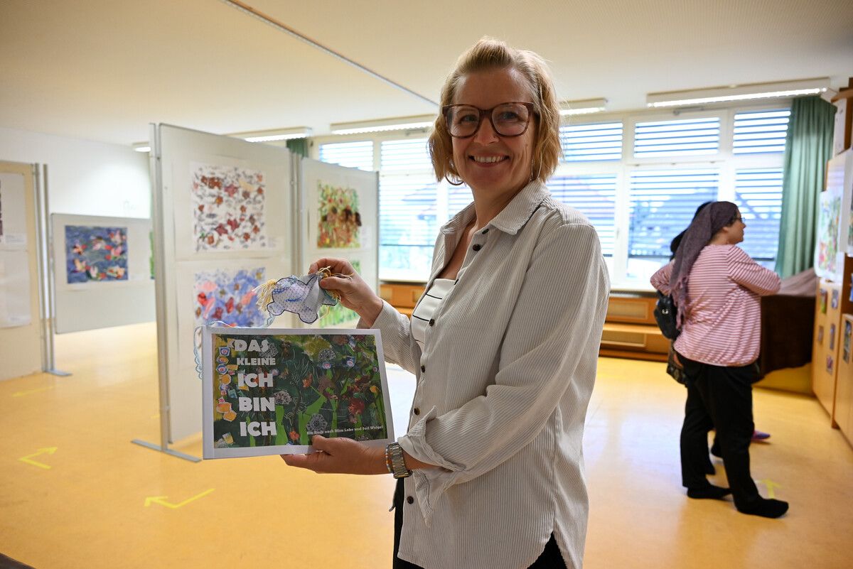 Kindergartenleiterin Silke Rezsnyak zeigt das eigens gemalte Werk inklusive selbst kreiertem „Ich bin Ich“. Jedes Kind erhält am Ende der Ausstellung sein ganz persönliches Exemplar.