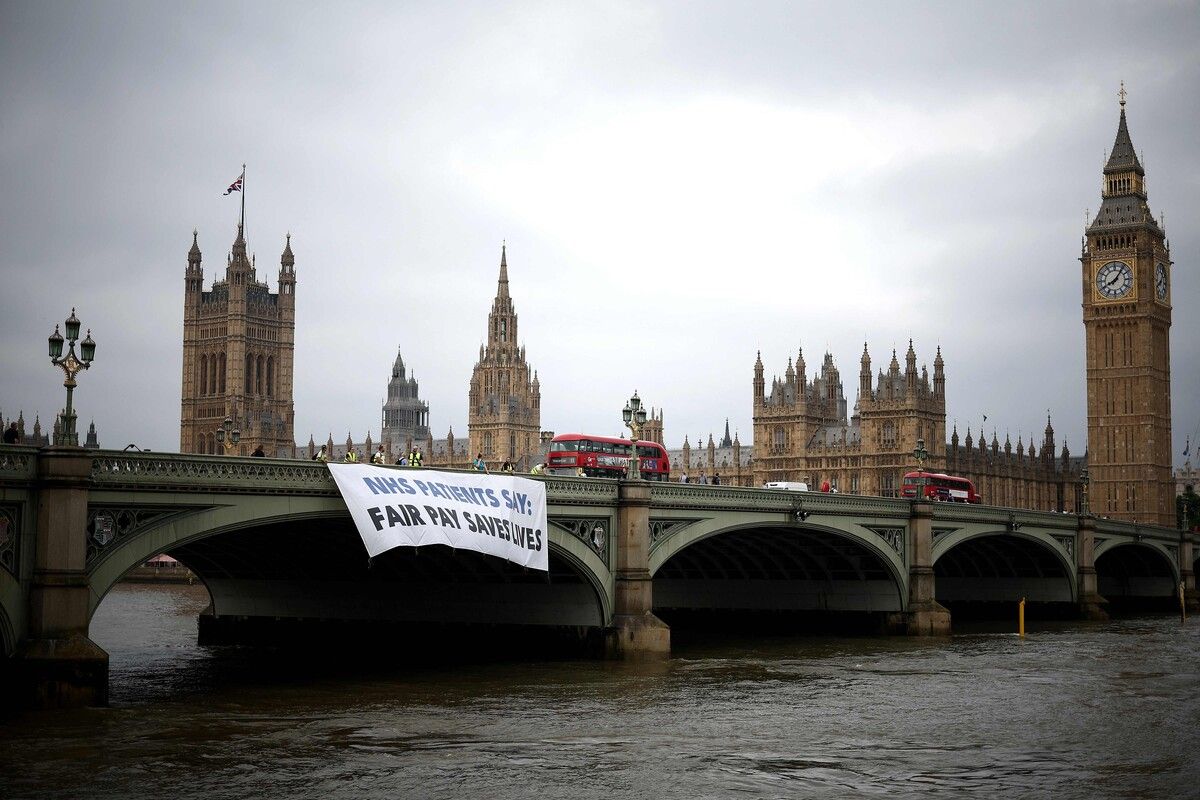Jungärzte protestieren mit einem Plakat vor dem britischen Parlament in London: Sie fordern mehr Gehalt und bessere Arbeitsbedingungen. AFP
