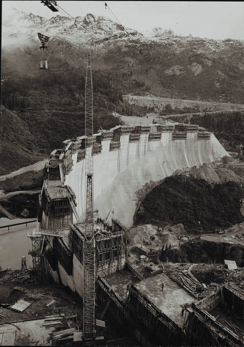 Die doppelt gebogene Kopsstaumauer umfasst eine Gesamtlänge von 614 Metern sowie eine Höhe von 122 Metern und gilt als wahres Meisterwerk der Statik.
              ⇒
              100 Jahre Illwerke; Oskar Spang, Stadtarchiv Bregenz; Ansichtskartensamlung, Vlbg Landesbibliothek