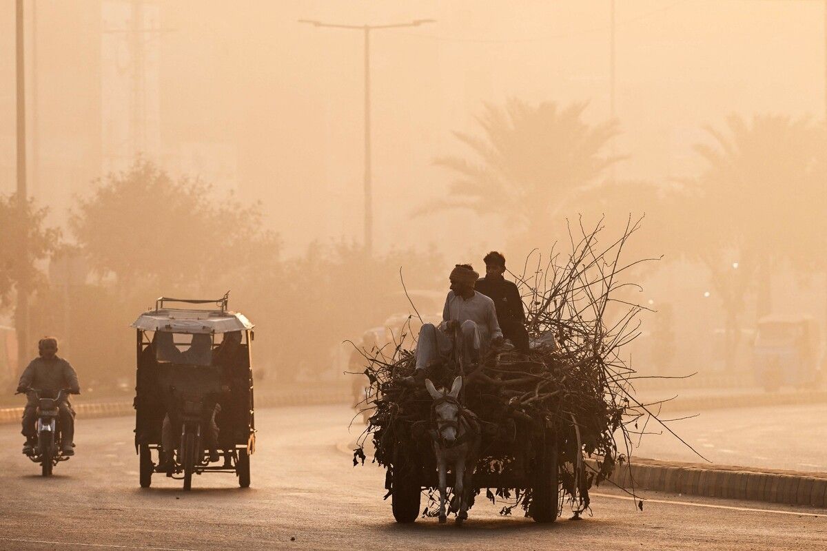 Männer fahren in Lahore (Pakistan) mit einer von Eseln gezogenen Karre eine von Smog umgebene Straße entlang. AFP