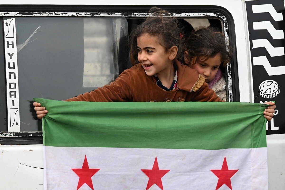 In Homs hält ein Mädchen in einem Bus mit heimkehrenden Syrern die Flagge Syriens, die seit Dezember 2024 verwendet wird, aus dem Fenster. AFP