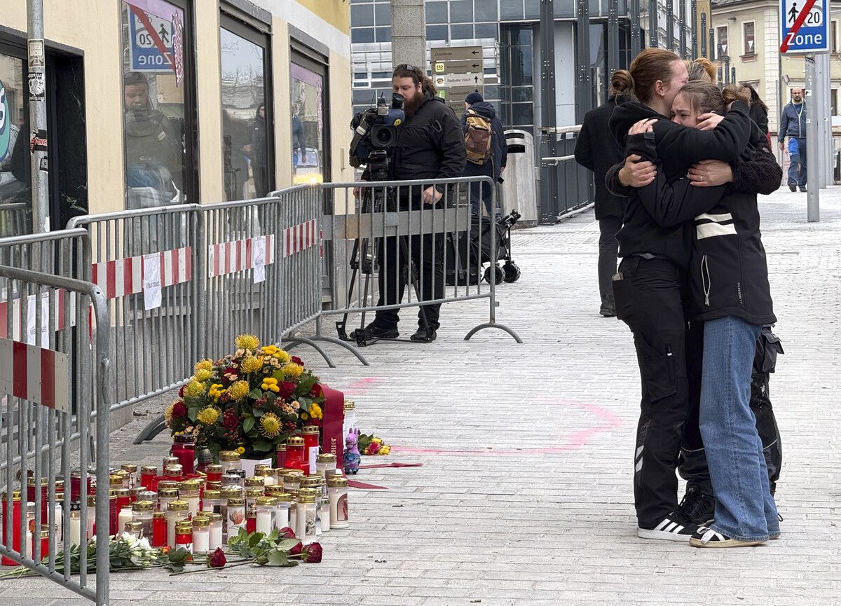 Trauernde umarmen sich am Tatort in Villach, wo Blumen und Kerzen niedergelegt wurden. ⇒APA/Eggenberger