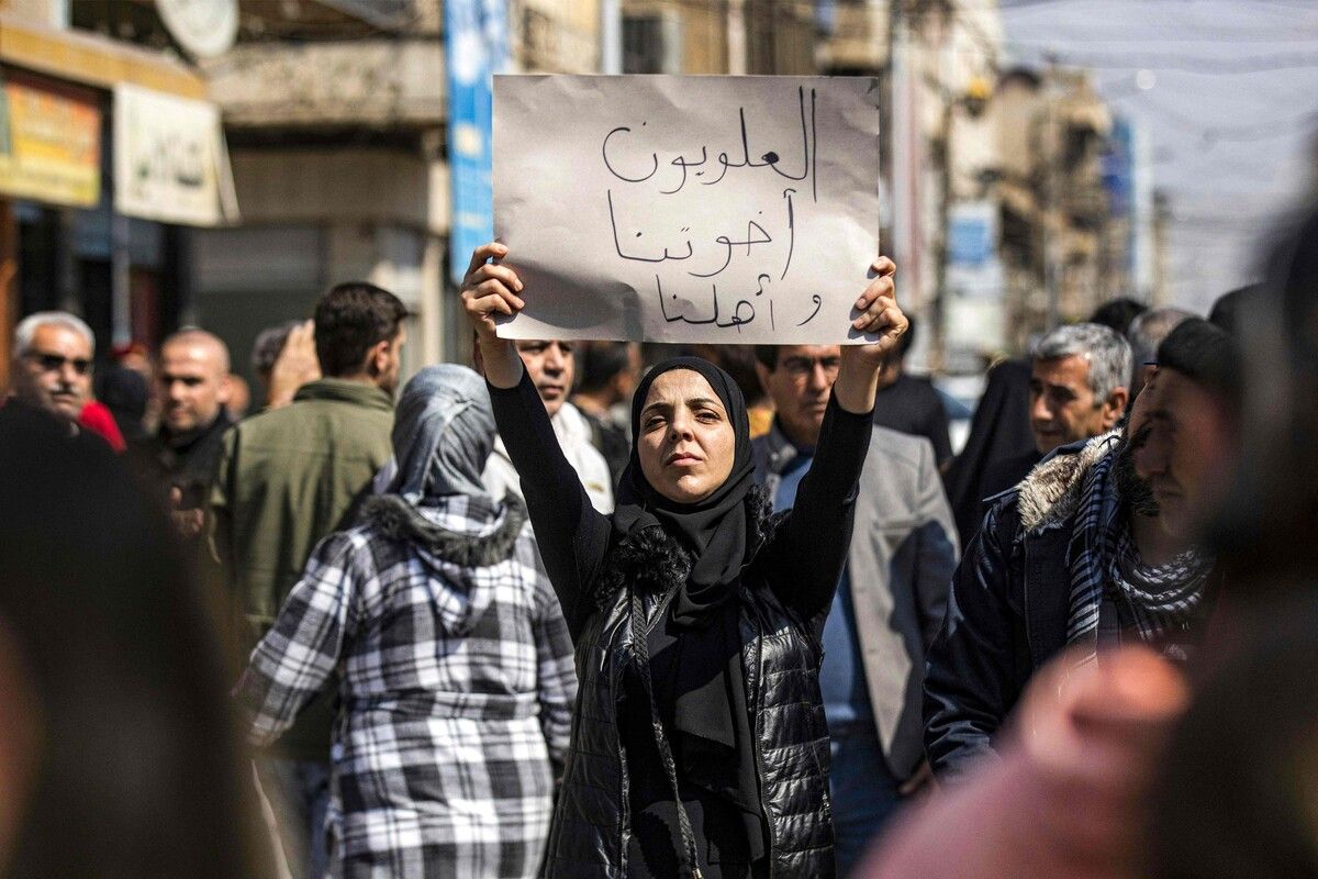Eine Frau hält ein Schild mit der Aufschrift „Alawiten sind unsere Brüder und unsere Familie“ bei einer Demo in der syrischen Stadt Qamishli. afp