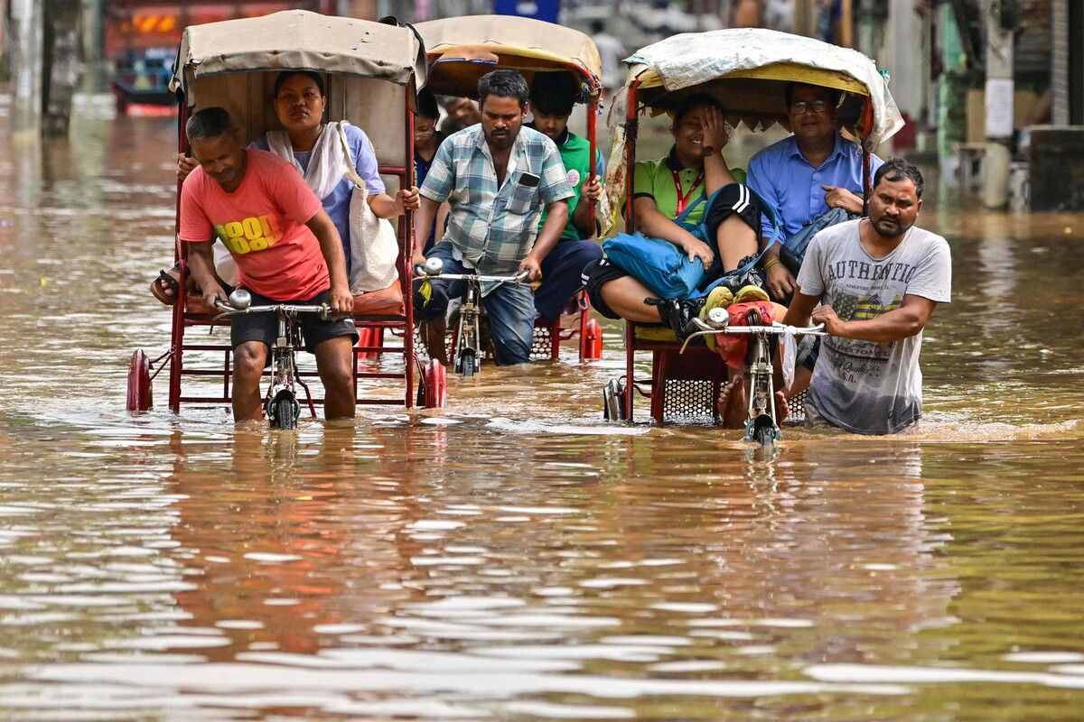 Einheimische fahren mit Fahrradrikschas durch eine überschwemmte Straße nach schweren Regenfällen in Guwahati.