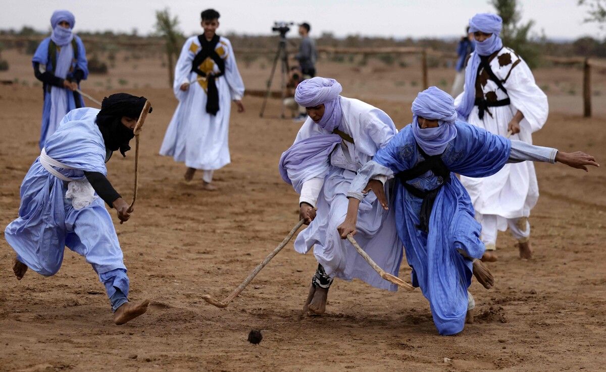 Marokkanische Nomaden in traditionellen Gewändern spielen während des Nomadenfestivals in Mhamid El-Ghizlane in der südlichen Sahara-Wüste Sandhockey.