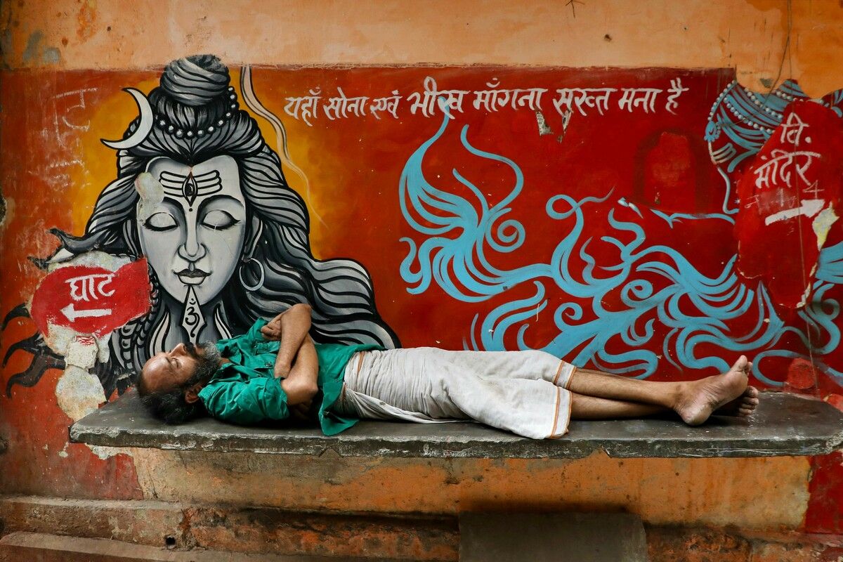 Ein Mann schläft neben einem Wandgemälde der hinduistischen Gottheit Shiva in der indischen Stadt Varanasi.