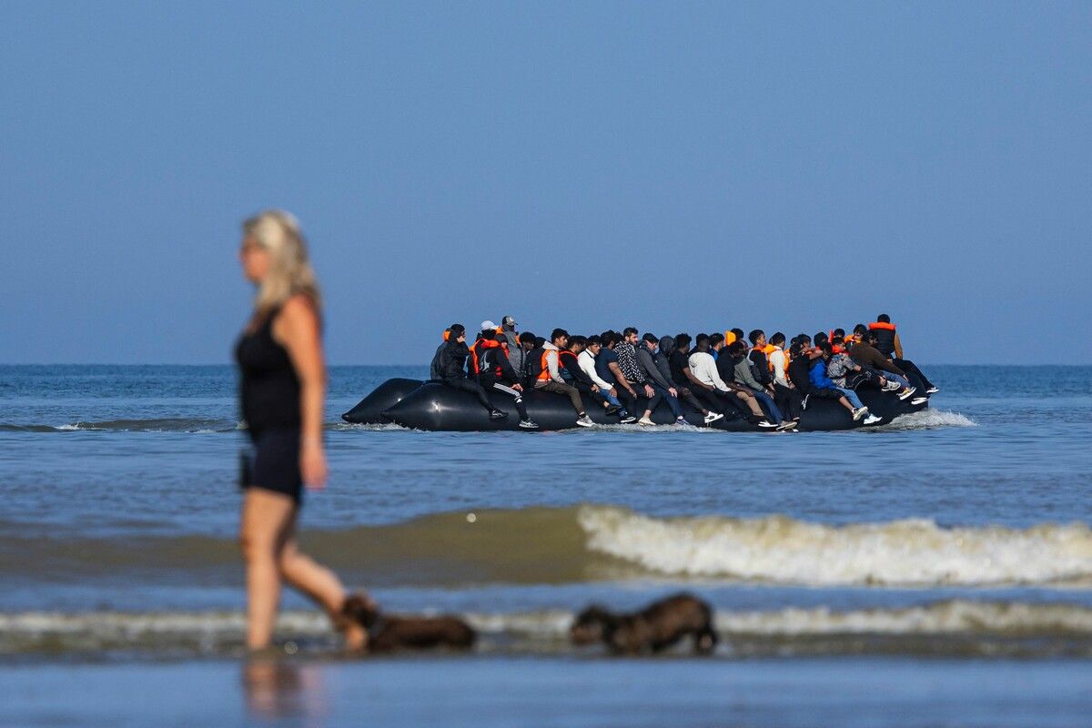 Eine Touristin geht mit ihren Hunden am Strand von Hardelot spazieren, während im Hintergrund Migranten dichtgedrängt auf einem Boot versuchen, den Ärmelkanal zu überqueren. AFP (5)