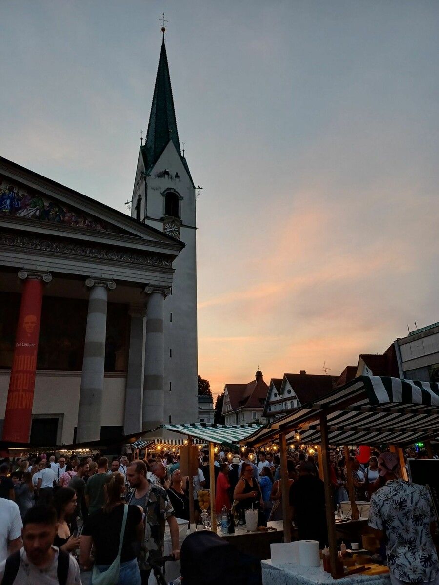 Gäste zwischen Ständen und Musik, ein lebendiger Marktplatz vor der Kirche.⇒SOR
