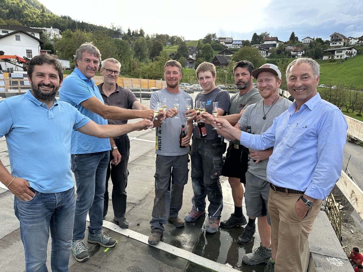 Bauamtsmitarbeiter Bertram Schmid und Bauamtsleiter Robert Hartmann feiern mit Vertretern der Bauleitung und Handwerkern die abgeschlossene Rohbauphase. ⇒Marktgemeinde Frastanz