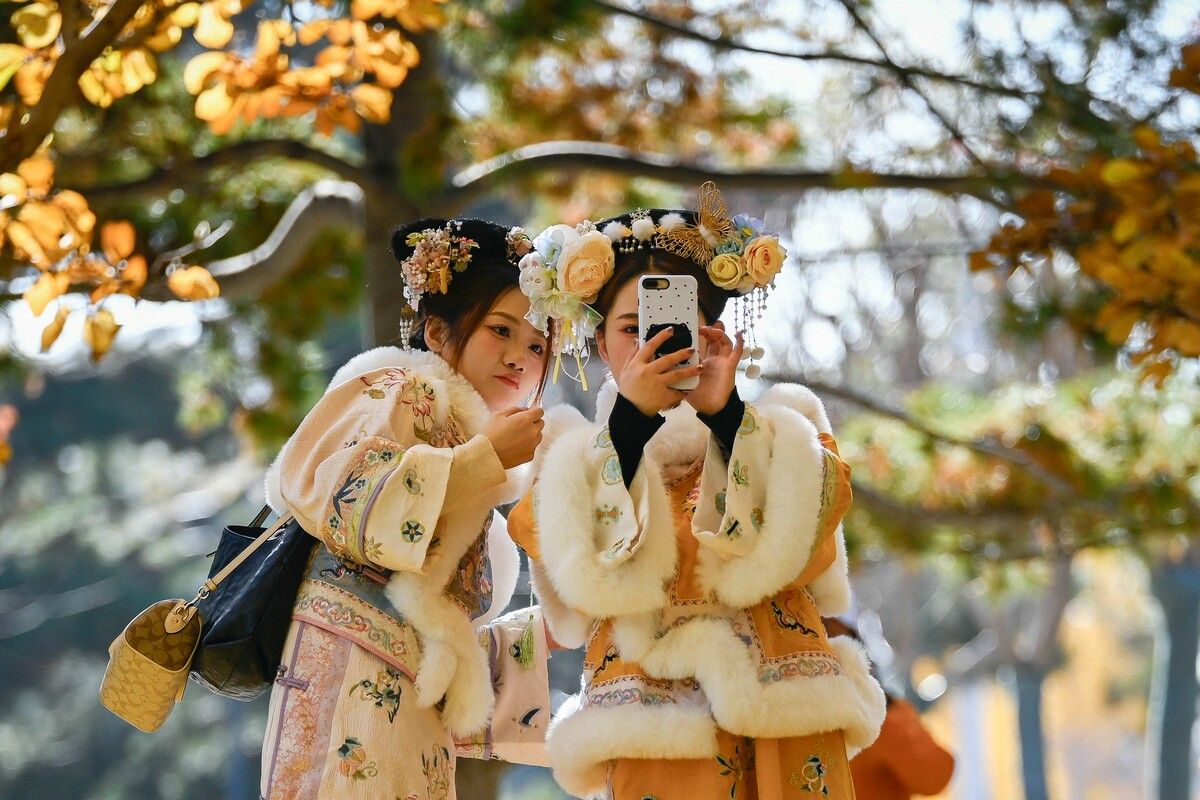 Zwei Frauen in traditioneller Kleidung machen ein Selfie beim Spaziergang auf einem Weg in Peking.