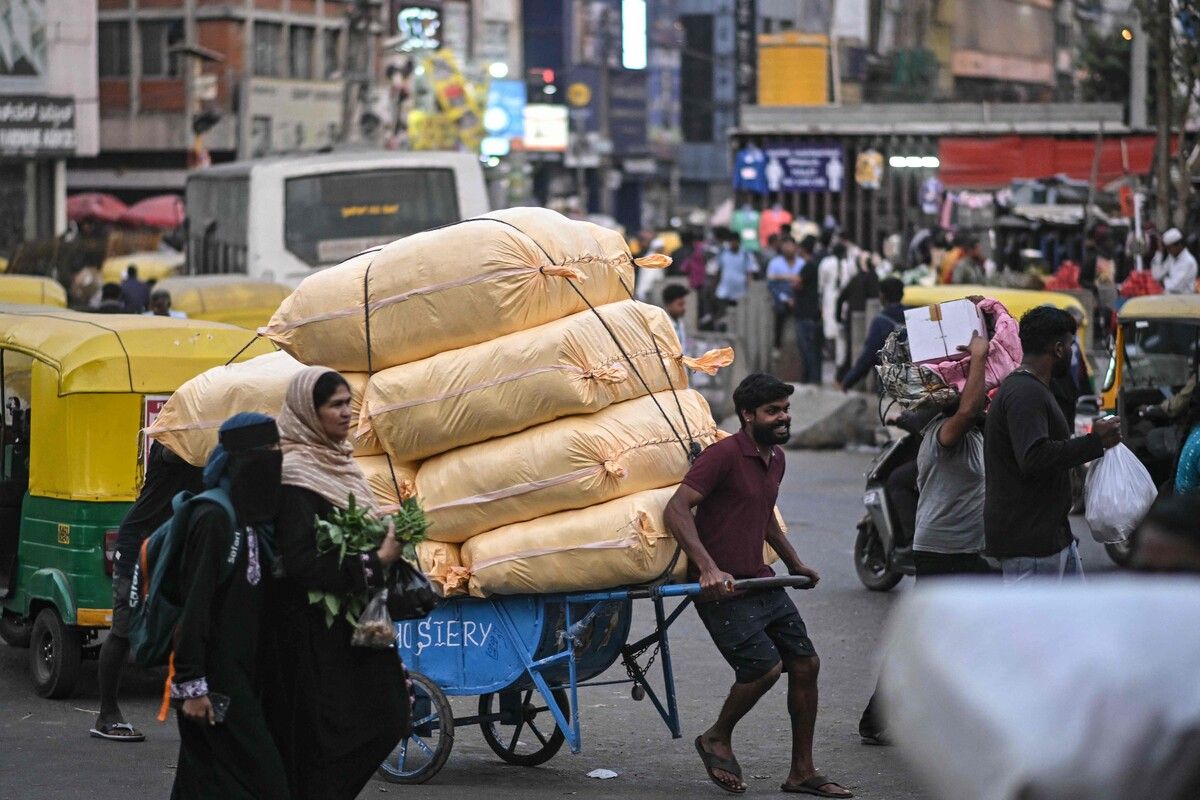 Ein Mann schiebt eine Schubkarre mit Waren durch einen vollen Markt in Bengaluru in Indien.
