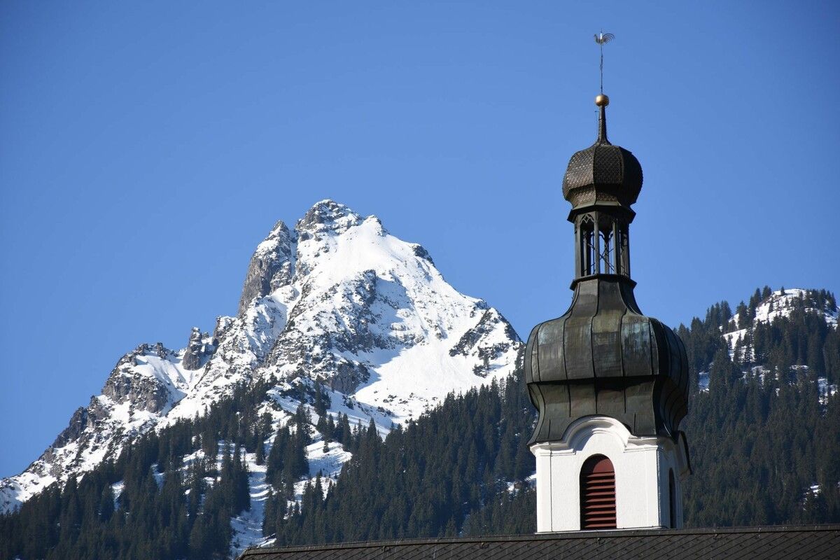 Eine Teilansicht des ungefähr 40 Meter hohen Turmes der Pfarr- und Wallfahrtskirche Tschagguns mit der Tschaggunser Mittagspitze (2167 m) im Hintergrund. ⇒SCO