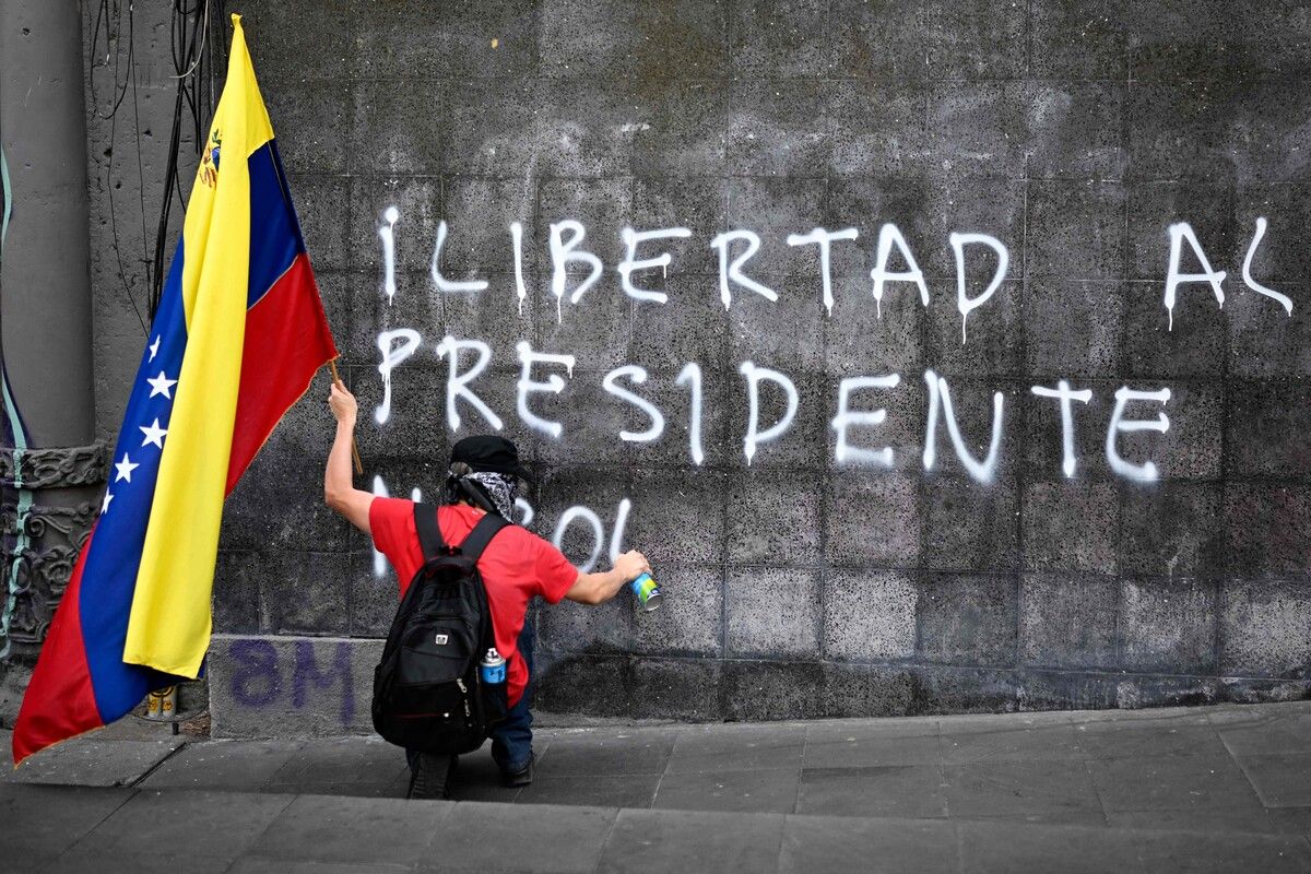 Ein Demonstrant mit venezolanischer Flagge malt in Mexiko‑Stadt ein Graffito „Freiheit für Präsident Nicolás (Maduro)“ an eine Wand.