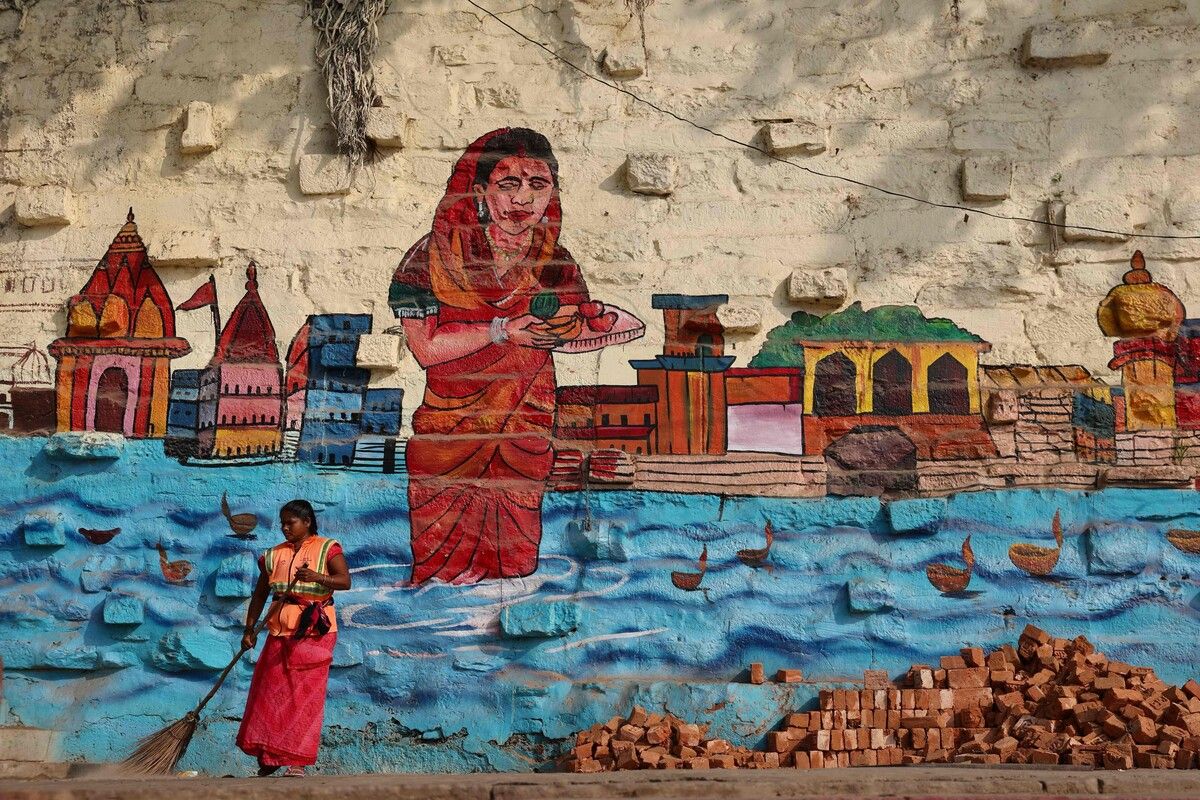Eine Frau fegt vor einem monumentalen Wandbild am Bundiparkota Ghat in Varanasi, das das Ufer des Ganges zeigt. AFP (5)