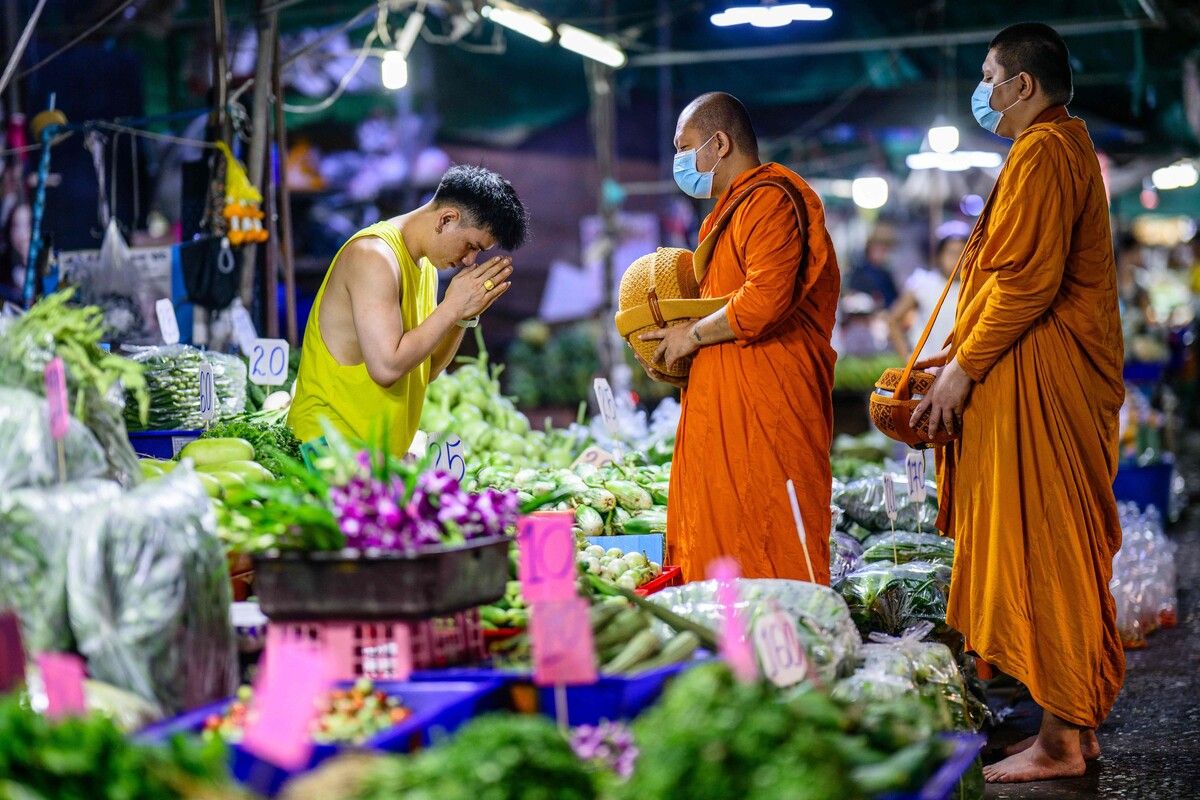 Eine Gemüsehändlerin verbeugt sich vor Mönchen beim Almosensammeln auf dem Khlong-Toei-Markt in Bangkok.