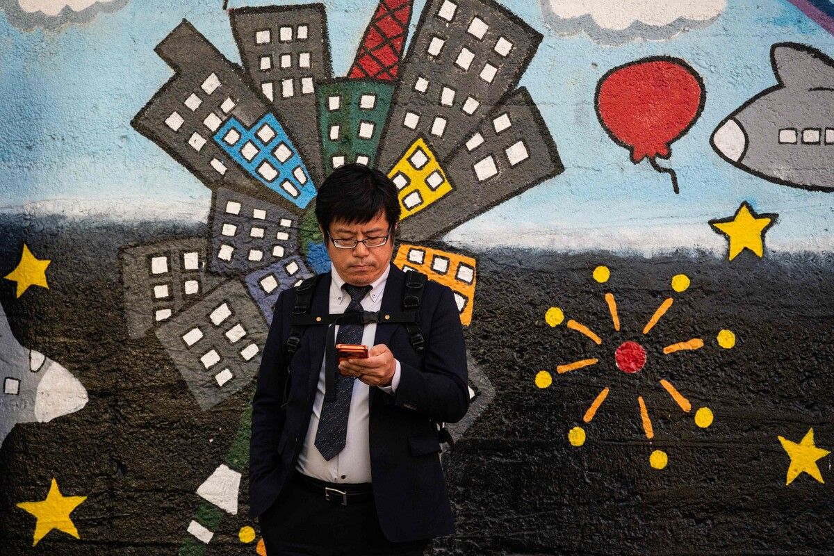 Ein Mann überprüft sein Handy vor einem Wandgemälde im Zentrum von Tokio.