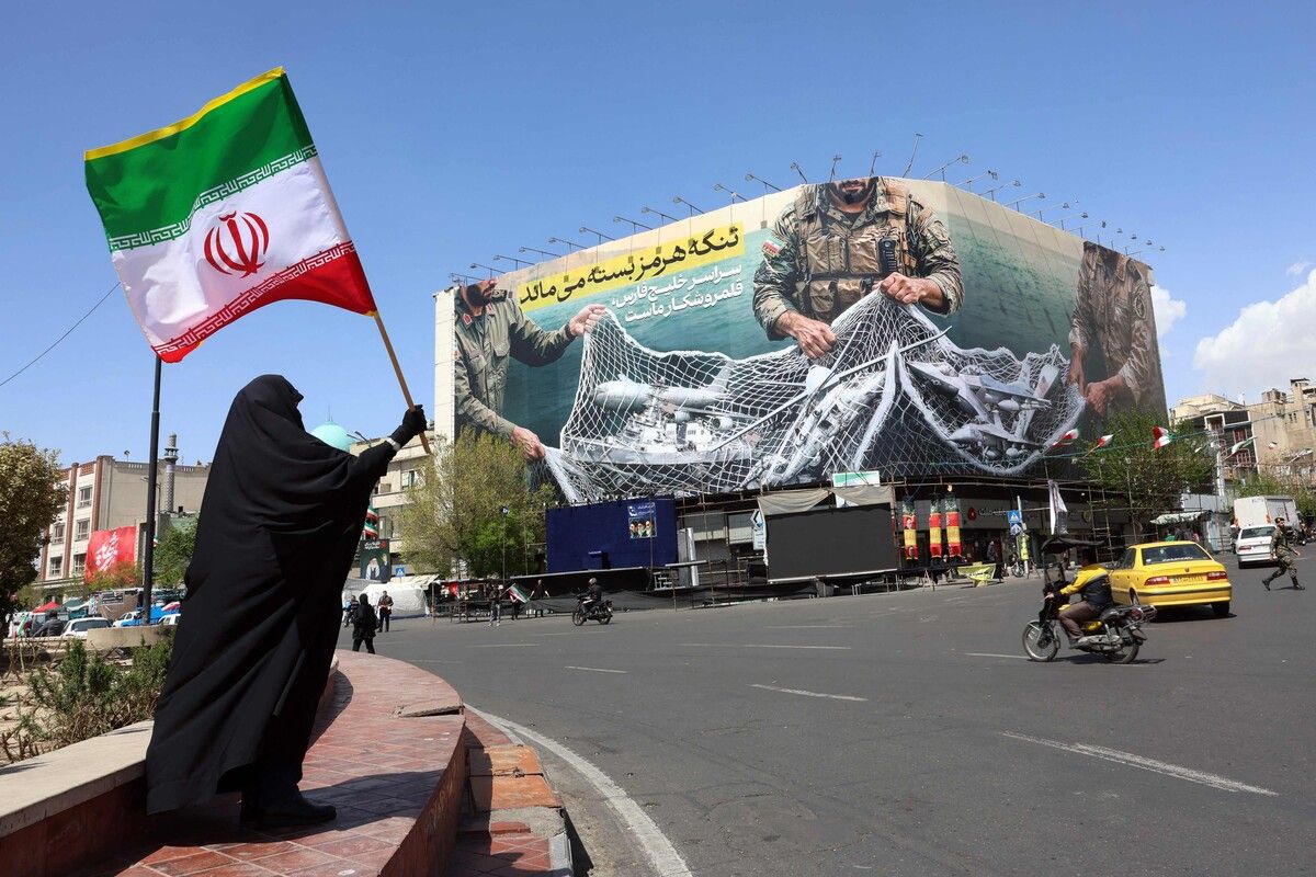 Eine Frau hält die iranische Flagge nahe einem Plakat „Straße von Hormus bleibt geschlossen“ am Enqelab-Platz in Teheran.