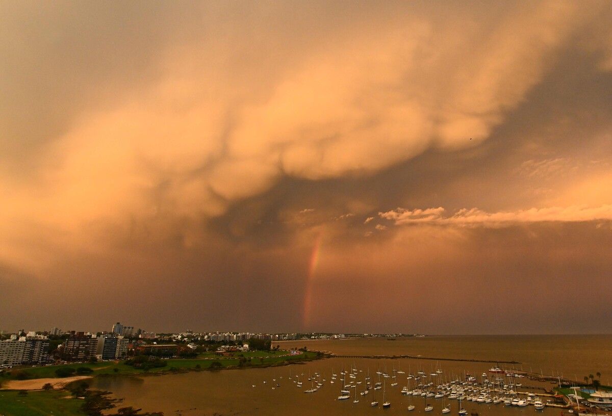In Montevideo in Uruguay ist ein Regenbogen und eine von der untergehenden Sonne beleuchtete Mammatuswolkenformation zu sehen.
