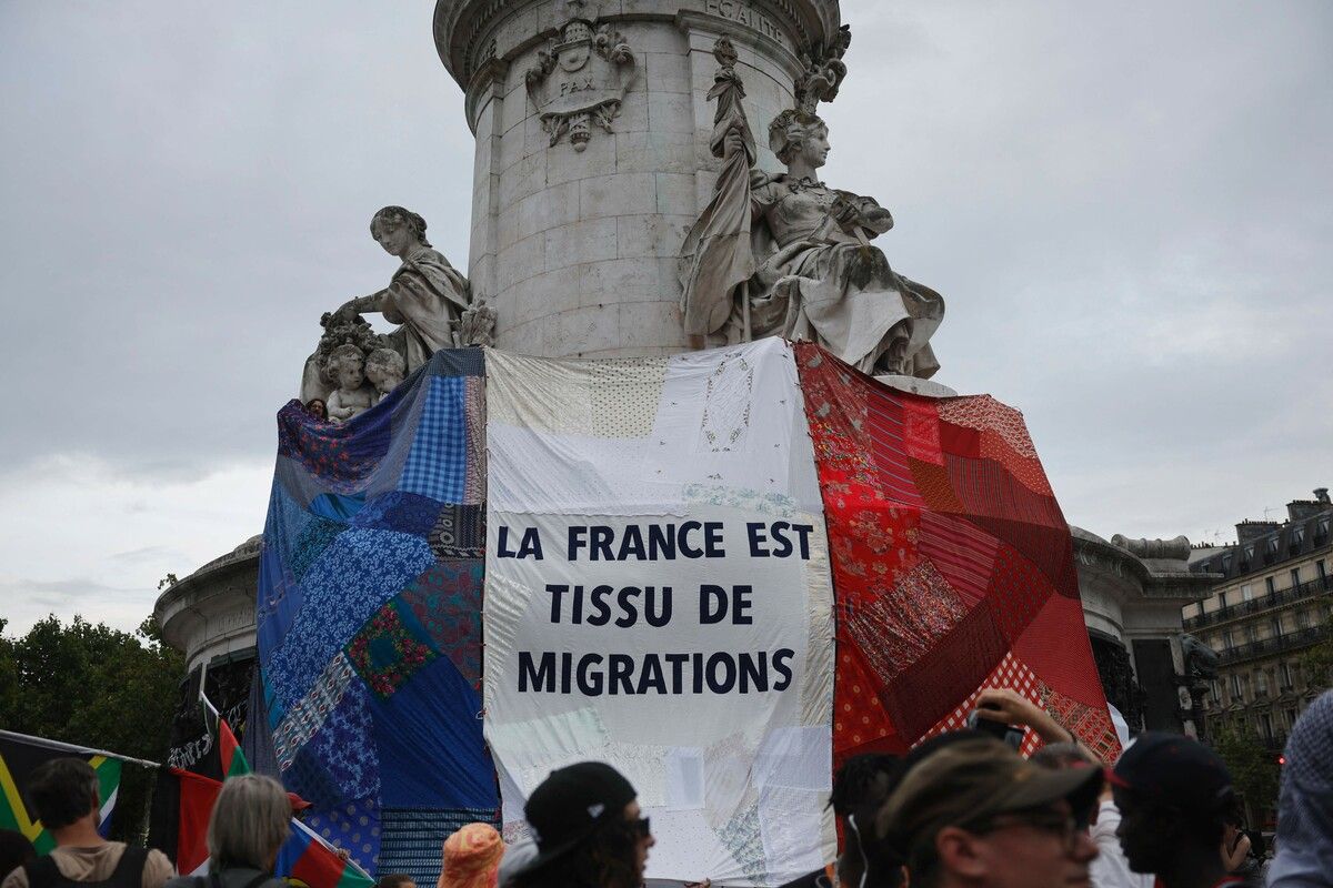 Das Foto zeigt das Republik-Denkmal in Paris, verhüllt mit einem Banner „Frankreich ist ein Migrationsgewebe“, während Demonstranten bei einer Gegenveranstaltung soziale Folgen der Olympischen Spiele hervorheben.