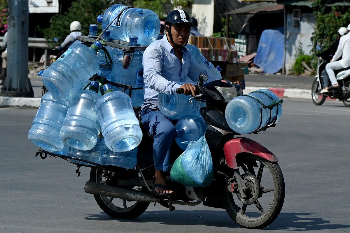 Ein Mann transportiert auf seinem Motorrad mehrere Wasserbehälter. Auch in Vietnam ist es derzeit extrem heiß.