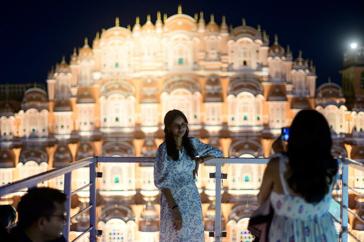 Eine Frau posiert vor der Kulisse des Wahrzeichens Hawa Mahal oder „Palast der Winde“ in einem Dachcafé im indischen Jaipur.