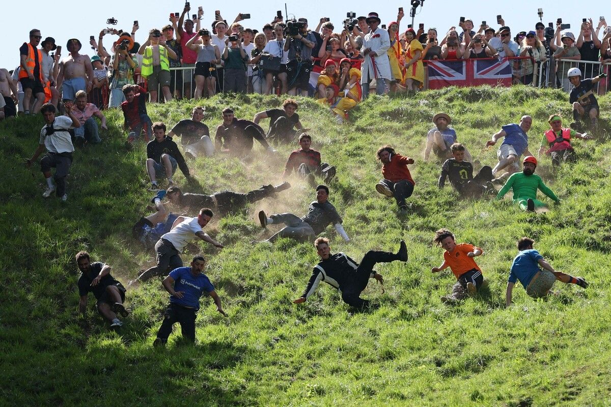 Tom Kopke, deutscher YouTuber und Sieger des ersten Männerlaufs, stürzt mit anderen Teilnehmern beim Cooper’s Hill Cheese Rolling einem rollenden Käse hinterher.